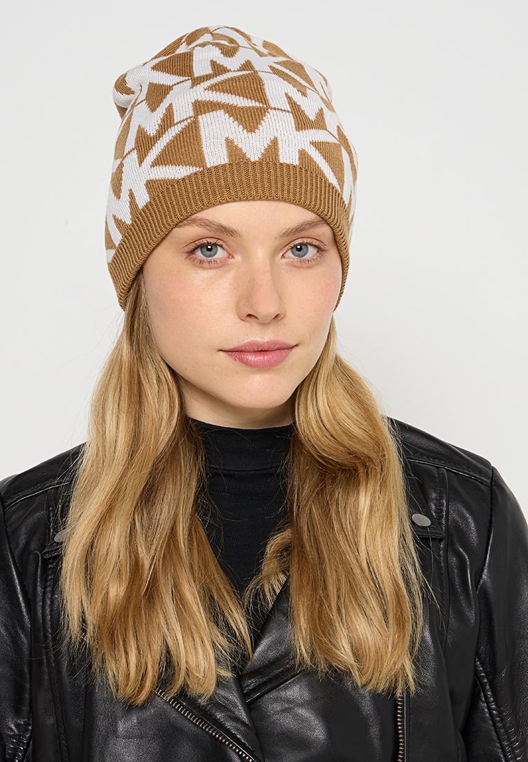 Brązowa i biała czapka dziana z geometrycznym wzorem, miękką teksturą i prążkowanym wykończeniem, noszona z czarną skórzaną kurtką.