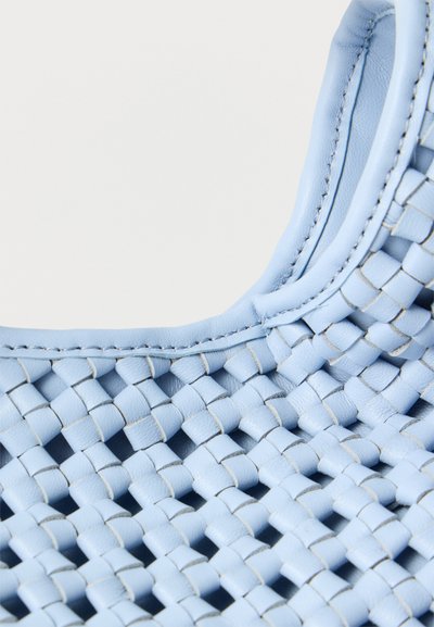 Κοντινό πλάνο λαβής τσάντας χειρός από ανοιχτό μπλε υφαντό δέρμα με λεπτομερείς ραφές και πλεγμένες λωρίδες δέρματος.