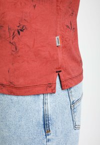 T-shirt rosso a maniche corte con stampa floreale nera, con uno spacco laterale all'orlo e un'etichetta in tessuto sul lato sinistro.