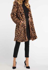 Plysjakke med leopardprint og en lang, løs silhuet, der har sidelommer og satinindvendig, suppleret med sorte tætsiddende bukser og højhælede sko.