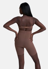 Brauner Shapewear-Body aus elastischem Material mit verstellbaren Trägern, in mittellanger Länge bis zum Oberschenkel und einem Haken- und Ösenverschluss im Rücken.