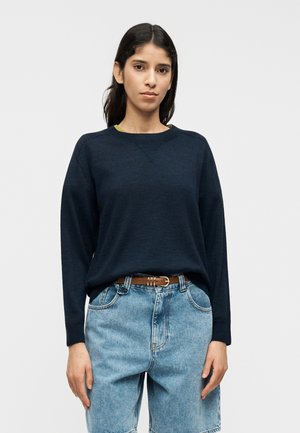 Μπλε ναυτικό φούτερ μακρυμάνικο με στρογγυλή λαιμόκοψη, σετ με ανοιχτό μπλε τζιν σορτς. Το ύφασμα φαίνεται μαλακό με χαλαρή εφαρμογή.