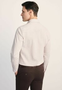 Jasno kolorowana koszula w kratkę uszyta z miękkiego materiału, posiadająca długie rękawy i wywinięty kołnierz, zestawiona z ciemnobrązowymi spodniami.