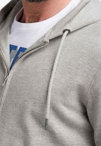 Felpa grigia con zip e coulisse. Tessuto morbido, tasca a marsupio, logo discreto sul petto, con zip argentata e cordini grigi texturizzati.