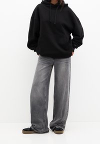 Svart hoodie med känguruficka, kombinerad med grå vida jeans och svarta sneakers med en tan sula. Enkelt design, inga mönster.