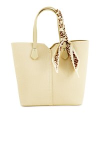 Beige totebag van textuurmateriaal, met twee handgrepen en een decoratieve sjaal die aan één kant is vastgemaakt. Hexagonaal hardware accentueert het ontwerp.
