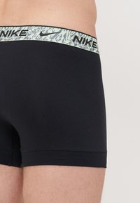Black boxer briefs made from soft fabric, featuring a light green patterned waistband with "NIKE" logo in black.