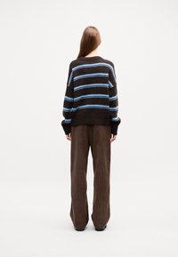 Braun gestreifter Pullover mit hellblauen horizontalen Streifen, kombiniert mit weit geschnittenen braunen Cordhosen. Weiche Textur, lässige Passform.