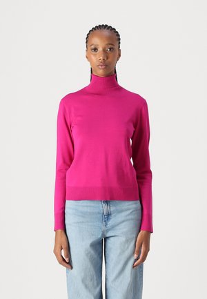 Fitted turtleneck sweater in bright pink, made of a soft fabric with ribbed cuffs and hem, paired with light blue jeans.