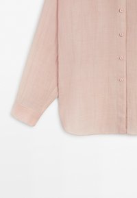 Lichtroze blouse met lange mouwen, knopen aan de voorkant en een enkele manchet aan de zichtbare mouw.