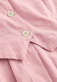 Gros plan sur un tissu rose avec deux boutons couleur crème cousus, montrant la texture et les détails de couture.