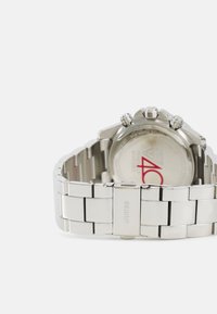 Montre en acier inoxydable argenté avec un bracelet à maillons, présentant un cadran rond, trois couronnes et un cadran blanc avec un logo rouge.