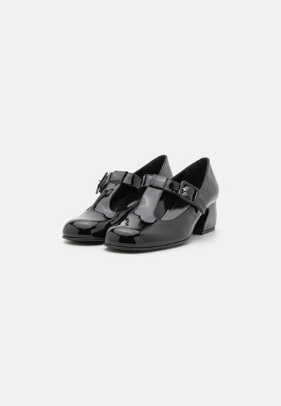 Zapatos de charol negros con punta redondeada, diseño de tira en forma de T y un pequeño tacón cuadrado. Presentan un accesorio decorativo de hebilla.