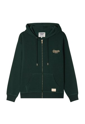 Sudadera verde con cremallera, hecha de tela suave, que presenta un bolsillo frontal, capucha con cordón y un logo bordado en dorado en el lado izquierdo del pecho.