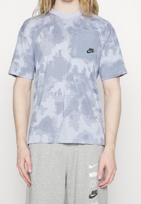 Gray and blue short-sleeve T-shirt with dotted pattern, featuring a zippered chest pocket and Nike logo. Cotton blend fabric, relaxed fit.