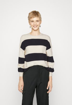 Striped knit sweater in cream and navy with a relaxed fit, round neckline, ribbed cuffs, and soft texture. Paired with black pants.
