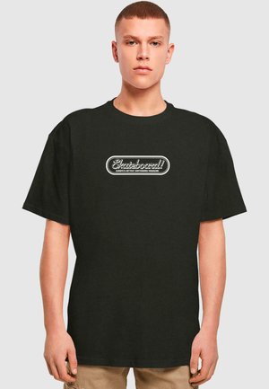T-shirt en coton noir avec un col rond, affichant un logo graphique blanc portant l'inscription "Skateboard !" centré sur la poitrine. Manches courtes.