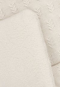 Plaid en crème, présentant un côté en polaire texturée et un côté en tricot avec des motifs de feuilles en relief. Matériaux doux et confortables.