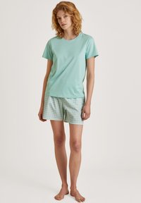 Mintgroene T-shirt met korte mouwen en een ronde hals, gecombineerd met lichtblauwe shorts met een geometrisch patroon.