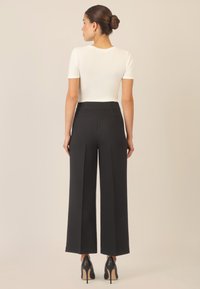 Pantalons larges noirs à taille haute, avec des plis soignés et une texture lisse. Portés avec un haut ajusté à manches courtes blanc et des talons noirs.