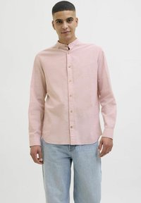 Ljusrosa långärmad skjorta med mandarin-krage och knappstängning fram, i kombination med ljusblå jeans. Slät tygstruktur, avslappnad passform.