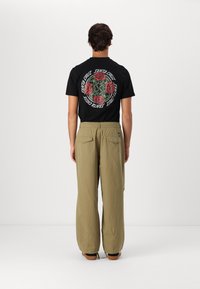 Black t-shirt featuring a colorful floral graphic on the back, paired with loose-fitting beige pants. Both garments are casual in style.