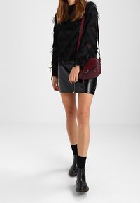 Zwart langärmlig top met gestructureerd ontwerp; glanzende zwarte leren minirok; bordeauxrode schoudertas; zwarte enkellaarsjes; donkere sokken.