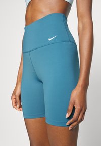 Szorty sportowe z wysokim stanem w odcieniu teal, wykonane z elastycznej tkaniny. Posiadają gładki pas i białe logo Nike.