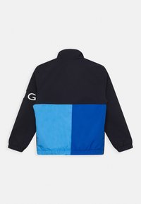 Farbblockierte Jacke in Marineblau und zwei Blautönen. Leichter Stoff mit elastischen Bündchen und hohem Kragen. Logo am Ärmel.