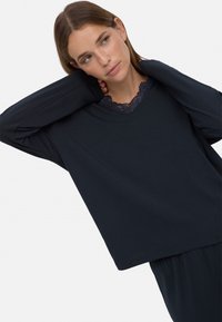 Top de manga larga en color navy con escote en V y borde de encaje, hecho de una tela suave, con un corte relajado y hombros caídos.