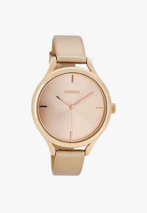 Montre ronde avec un boîtier en métal doré rose, un cadran métallique rose et un bracelet en cuir beige doux. Présente des marqueurs d'heure minimalistes.