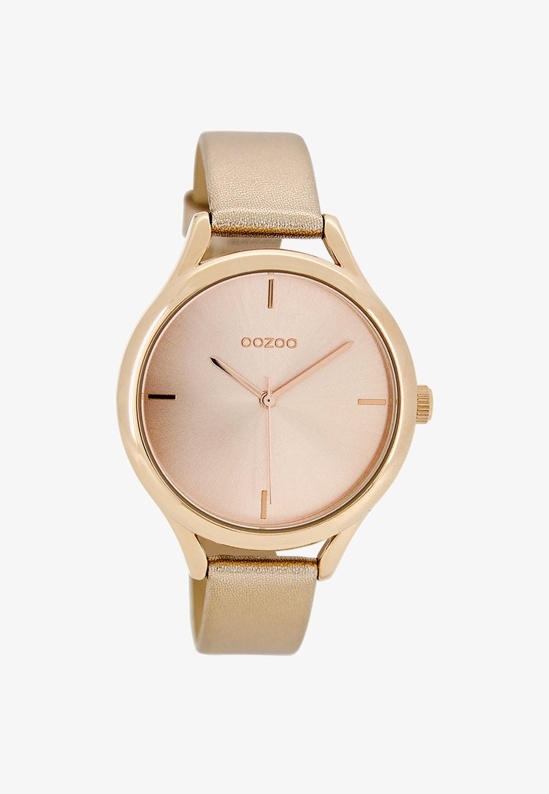 Montre ronde avec un boîtier en métal doré rose, un cadran métallique rose et un bracelet en cuir beige doux. Présente des marqueurs d'heure minimalistes.