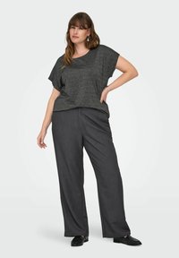 Haut gris métallisé à manches courtes associé à un pantalon large taille haute gris foncé. Le mannequin se tient avec une main sur la hanche, portant des chaussures noires.