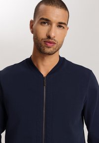 Chaqueta bomber de marina con cuello acanalado y cremallera completa. Tejido suave sin patrones visibles. Diseño moderno y ajustado.