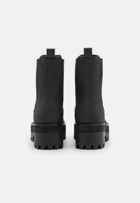 Botines negros hasta el tobillo con un acabado suave y mate, paneles laterales elásticos y una suela gruesa y texturizada. Diseño recto y alto con tiradores traseros.