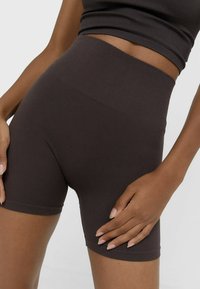 Pantaloni corti a vita alta di un marrone scuro a coste, con una texture liscia, caratterizzati da un design aderente che arriva fino a metà coscia.