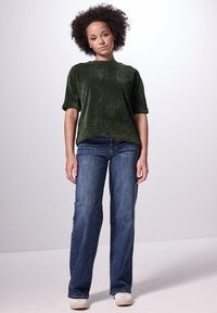 Camisa corta de manga verde y texturizada, combinada con jeans de pierna ancha azul y zapatillas blancas. Diseño sencillo sin estampados ni adornos.