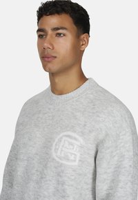 Jasnoszary sweter o splotach z okrągłym dekoltem, z delikatnym logo w dolnym lewym rogu. Miękka tekstura i luźny krój.