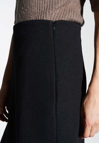 Gonna nera con una finitura liscia e texturizzata e uno spacco laterale, abbinata a un maglione rigato marrone chiaro. Presenta una cerniera discreta.