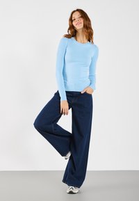 Lichtblauwe geribbelde lange mouwtop gecombineerd met donkerblauwe wijde jeans, aangevuld met witte sneakers. Soepele textuur en aansluitend ontwerp.