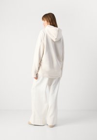 Beige hoodie with a drawstring hood, relaxed fit, soft texture, paired with wide-leg white trousers. Minimal design with no visible patterns.