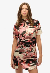 Vestido mini con estampado floral, de cuello alto y detalle de ojal. Presenta colores rosa, rojo y negro en una tela similar a la seda.