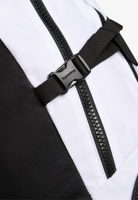 Sac à dos noir et blanc en tissu résistant, avec une fermeture éclair bien visible et une sangle texturée dotée d'une boucle en plastique noir portant l'inscription "Superdry".