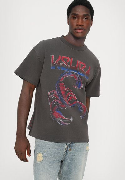 Tricou gri cu un grafic mare de scorpion roșu și albastru. Mâneci scurte, guler rotund și croială lejeră. Purtați cu blugi deschiși, distruși.