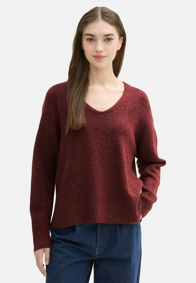 Bordeaux gebreide trui met een V-hals, geribde manchetten en zoom. Heeft een relaxte pasvorm en een zachte textuur, gecombineerd met donkerblauwe jeans.