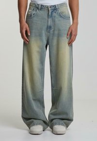 Reilut denim-farkut vaaleansinisinä, joissa on haalistuneita keltaisia yksityiskohtia. Ominaisuuksiin kuuluu klassinen viiden taskun muotoilu, napitus ja näkyvät ompelut.