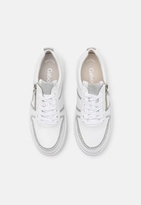 Baskets en cuir blanc avec des accents gris, à bout rond, avec fermeture à lacets et à zip, ornées de clous décoratifs sur le côté.