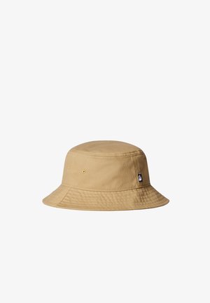 Sombrero tipo bucket de algodón beige con ala cosida y dos ojetes de ventilación a cada lado, con una pequeña etiqueta de marca en blanco y negro.