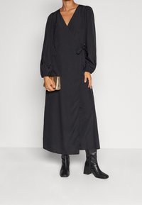 Svart omlotklänning med långa puffärmar, djup V-ringning och knytmidja. Kombinerad med en metallisk väska och knähöga svarta stövlar.