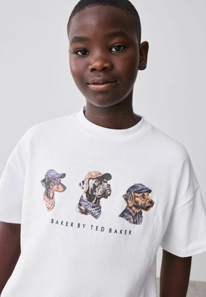 Junge trägt ein weißes T-Shirt mit Illustrationen von drei Hunden in Hüten und Schals, der Text "Baker by Ted Baker" unter den Illustrationen.